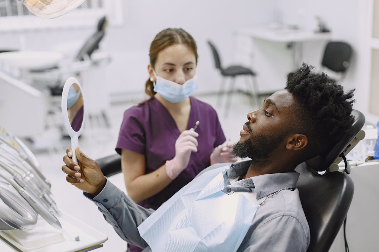 A man in a dental chair during a checkup with a professional dentist using a mirror.